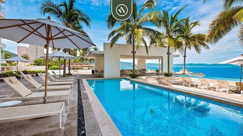 Shimmering outdoor swimming pool area flanked by pristine white lounge umbrellas and lush palm trees.
