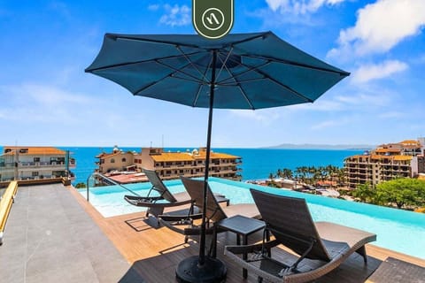 Stunning rooftop pool area featuring comfortable lounge chairs, a large shade umbrella, and sweeping views of the ocean and cityscape.