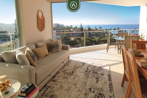 Relax in this bright living area featuring a plush sofa and a large area rug. The wide sliding doors open to a spacious balcony, offering an unobstructed, panoramic view of the sparkling ocean and tropical coastline.