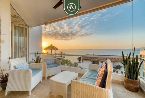 Cozy outdoor seating area with white wicker furniture and plush cushions, capturing a beautiful ocean sunset view.