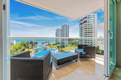Elegant high-rise balcony featuring dark wicker armchairs and a glass table, overlooking the complex pool and ocean.