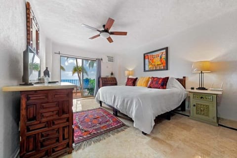 A cozy bedroom layout with colorful decorative pillows, a ceiling fan, and sliding glass doors that open to a scenic view.