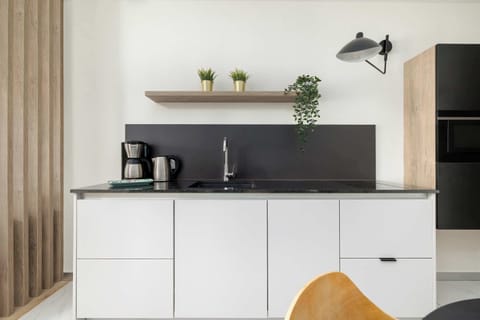 A modern kitchenette with sleek black and white contrasts. Open shelves display plants and tableware.