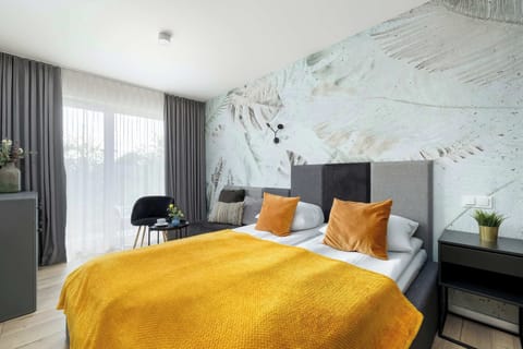 A cozy bedroom area with a double bed, yellow blanket, and marble-patterned accent wall. A small table and chair complete the space.