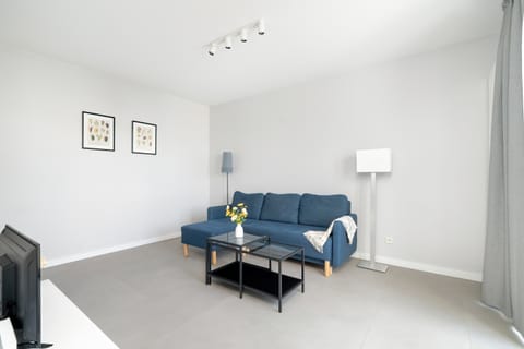 A modern living room with a blue sofa, coffee table, and minimalistic décor in neutral tones.