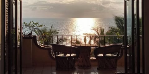 Scenic terrace patio seating facing directly into a bright sun flare over the shimmering ocean water.
