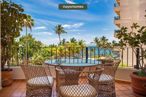 A private outdoor terrace featuring a glass-top table and woven chairs, overlooking palm trees and the sea.