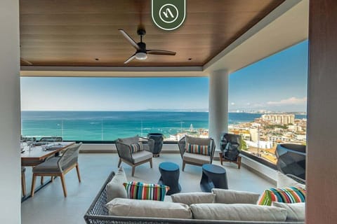 Expansive outdoor terrace highlighting luxury lounge seating arrangements, colorful accent pillows, and an incredible view of the bright blue sea.