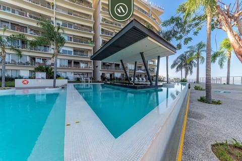 A vibrant look at the expansive communal swimming pool, highlighting the modern covered swim-up bar pavilion and the luxury condo building.