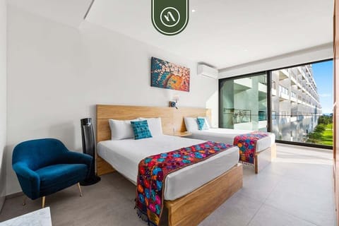 A bright, airy bedroom with two comfortable beds accented by colorful textiles. Large floor-to-ceiling windows offer direct access to a private balcony.