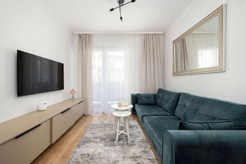 The spacious living area features a plush green sofa, flat-screen TV, and contemporary decor, creating a cozy space to relax or entertain guests.
