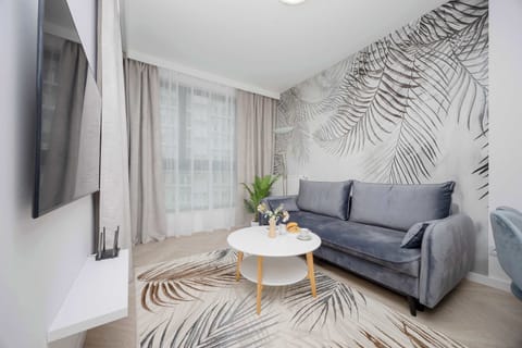 A cozy living room with a grey sofa, patterned accent wall, and a round coffee table – perfect for relaxing after a long day. Floor-to-ceiling curtains provide privacy and a soft, elegant touch.