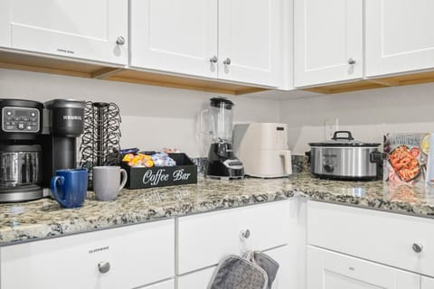 Charming coffee bar setup on gleaming granite countertops, complete with Keurig, mugs, and snacks. A cozy corner perfect for morning brews or hosting guests, blending functionality with personality in this well-appointed kitchen space.
