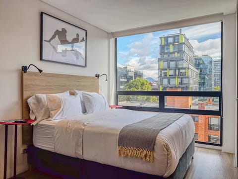 Room with double bed and large window with urban view