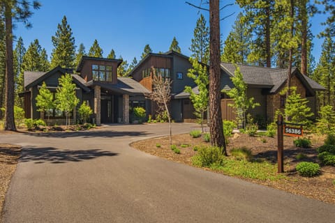 A spacious mountain retreat nestled among towering pines, featuring modern architecture with stone accents and large windows. The property offers a peaceful forest setting with ample parking and well-maintained landscaping, welcoming guests to a private wo