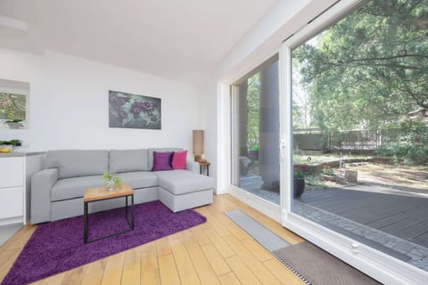 A spacious living room with large windows, a bright sofa, and a view of the green garden.