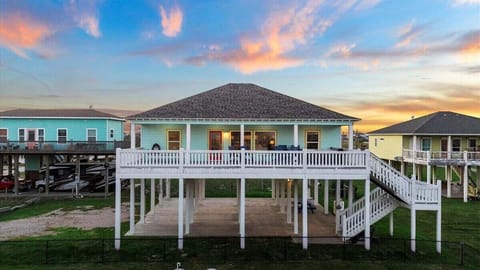 Elevated coastal vacation home on Bolivar Peninsula featuring a spacious wraparound deck, covered outdoor living space, and beautiful sunset skies near the Gulf Coast.