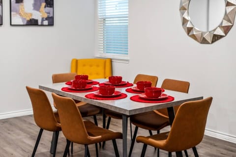 Modern dining area set for six, featuring a sleek table and vibrant red dishware. Comfortable chairs create a cozy spot for family meals or gatherings. Bright and inviting, this space is perfect for enjoying meals together during long-term stays.