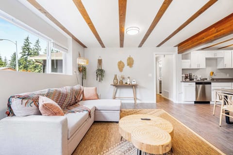 Modern open-concept living space featuring an L-shaped dove gray sofa with vibrant throw blankets and blush pillows, centered around a unique live-edge coffee table with visible wood grain.
