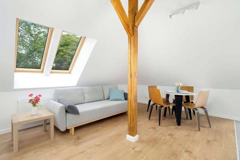 A bright attic living space with a grey sofa, small coffee table, and a skylight letting in natural light. Wooden beams add a rustic charm to the modern decor.