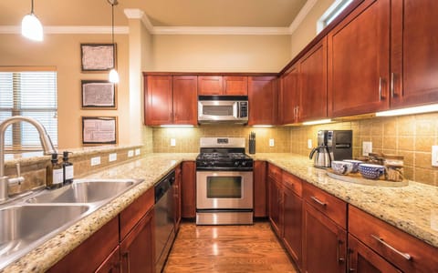 View of kitchen sink, dishwasher, oven, microwave, coffee maker, mugs and coffee grounds, sugar and half and half 