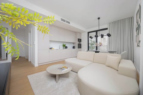 A bright living room with a large white sofa and a modern coffee table, decorated with plants and natural light.
