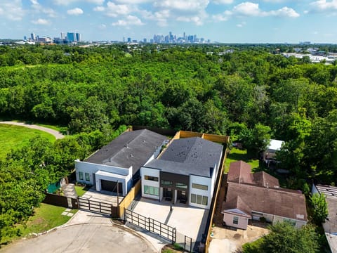 An aerial view of two modern gated properties surrounded by lush greenery, with the city skyline visible in the distance.