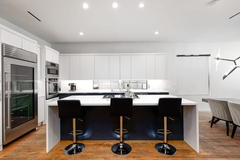 Modern kitchen with a large island, sleek white cabinets, stainless steel appliances, and three black bar stools.