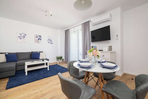 A modern living room with a gray sofa, round dining table, and large windows letting in natural light. Perfect for relaxing or sharing meals with loved ones.