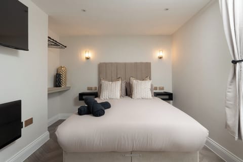 A bright, open-plan studio featuring a comfortable double bed, Smart TV with Netflix, a dressing table that doubles as a vanity and work desk, and a dedicated clothes hanging area—ideal for relaxing, working, or getting ready for the day.

