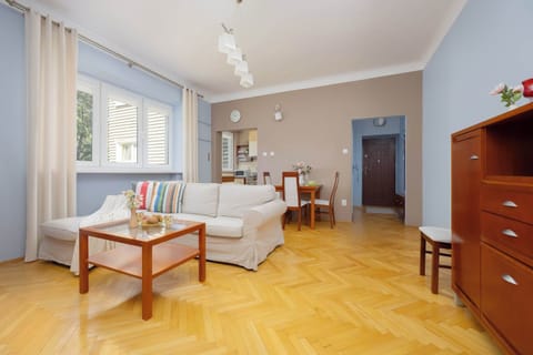 A bright living room with wooden flooring, a table, chairs, and a large window letting in natural light.