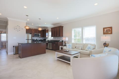 Spacious living area in the three bedroom home featuring a modern kitchen and cozy seating with beach decor and natural light