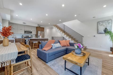 A modern, cozy living room with a plush sectional, warm neutral palette, and layered textures. A 65` TV is mounted on a sleek media wall with hidden storage, creating a stylish, clutter-free space perfect for relaxation and entertainment.