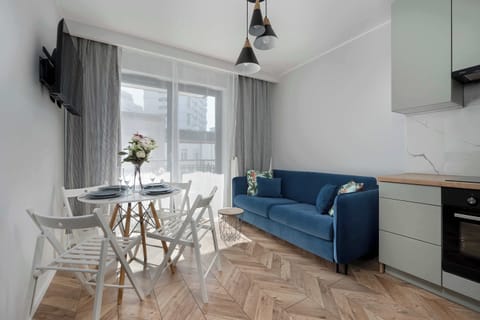 Cosy living room with blue sofa, soft cushions, and small dining table by the window, perfect for relaxing or sharing a meal.