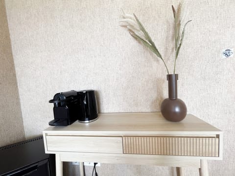 Stylish coffee corner with a modern espresso machine and decorative brown vase on a light wood table.

