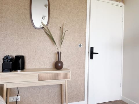 Warm and minimalist setup with a wooden console, brown vase, and oval mirror by a crisp white door.

