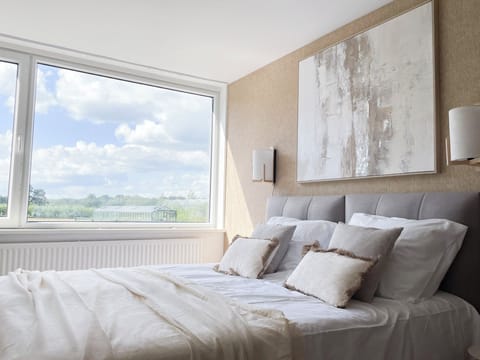 Cozy bed with layered pillows, natural tones, and warm daylight pouring through large windows.