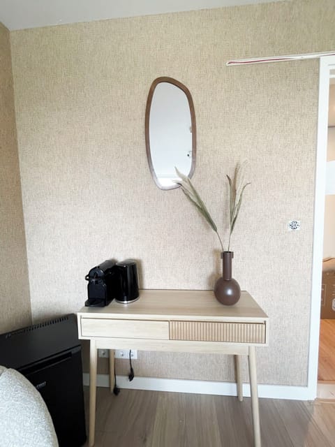 Sleek wooden console with a coffee setup, decorative vase, and soft lighting under an oval mirror.
