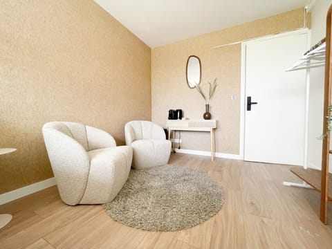 Modern lounge area with soft cream chairs, warm tones, a round rug, and a console with coffee setup and natural decor.