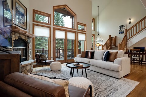Unwind in your spacious living room with soaring ceilings, stone fireplace, and forest views through floor-to-ceiling windows.