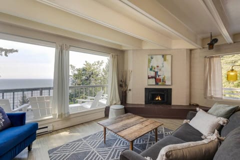 Gather in the cozy living room with big windows that frame peaceful views of the ocean and trees. Comfortable seating and warm touches make it a perfect spot to relax and enjoy time together.