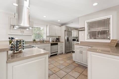U‑shaped kitchen featuring stainless appliances, vent hood, generous cabinetry, and a tiled floor