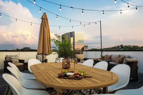 Rooftop dining table for six under string lights and an umbrella, set against the dusk skyline