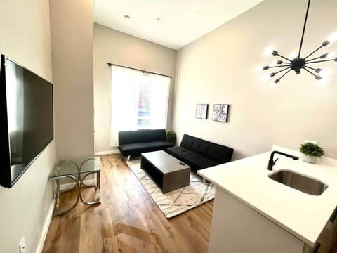 Living room with two futon sofa beds and a 50 inch TV, table connected to breakfast bar with stools and full kitchen.