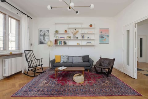 A colorful rug, a comfortable sofa and designer chairs create a cozy setting, while the wall with shelves full of books and decorations adds character for relaxing moments.