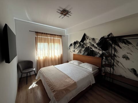 Sleep under the gaze of the Bucegi peaks in this stylish bedroom featuring a bold mountain mural, crisp bedding, and a wall-mounted Smart TV. A retreat that combines comfort and scenic inspiration.