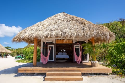 Thatched-roof beachfront teepee nestled in tropical greenery with hammock swings.