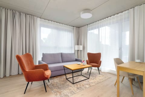 The cozy living room is filled with natural light from wide windows, with comfortable orange armchairs creating a perfect spot to relax.