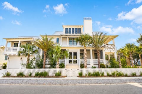 Stunning coastal home with elegant white facade, palm-lined entrance, and modern architectural details in a peaceful residential setting.