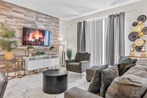 Unwind in this stylish living room with a cozy fireplace and a textured wood accent wall. The plush gray seating invites relaxation, while large windows with elegant curtains fill the space with natural light.